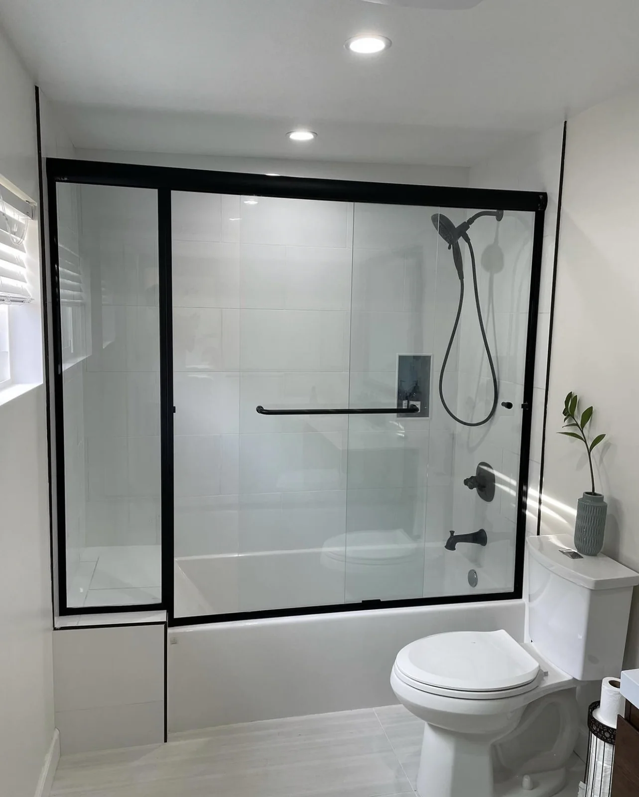 Bathroom with white tile, a black-framed glass tub enclosure and matching dark fixtures