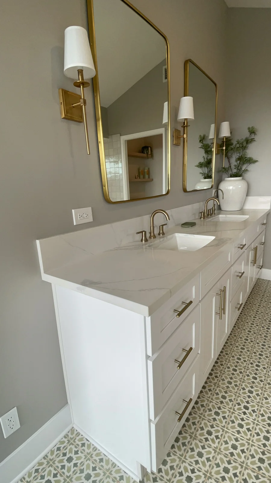 Long white double bathroom vanity with gold-framed mirrors, sconces and patterned floor tile