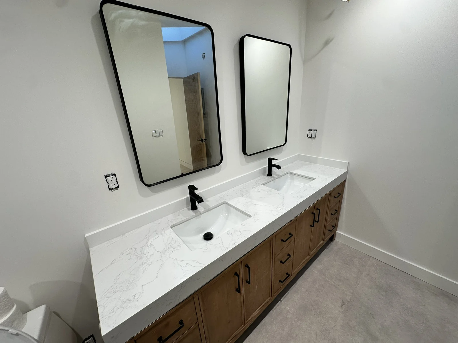 Finished bathroom double vanity with wood cabinetry, marble-look countertop, two sinks and black-framed mirrors