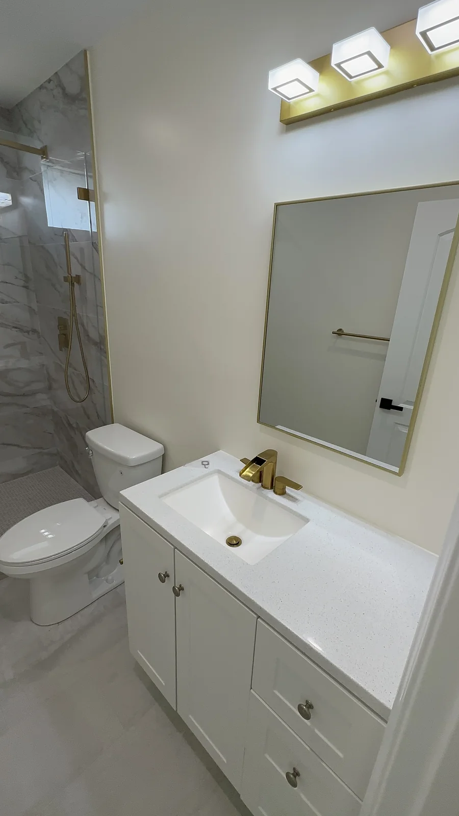 Finished bathroom vanity with gold-framed mirror, white countertop and gold fixtures