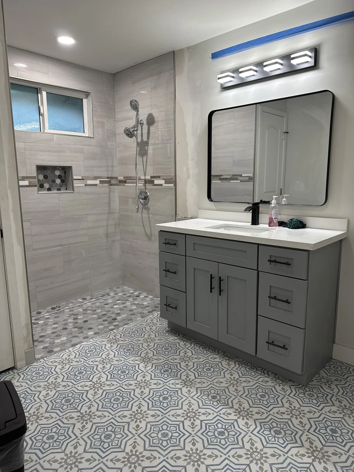 Gray bathroom vanity and shower during finishing work with patterned floor tile
