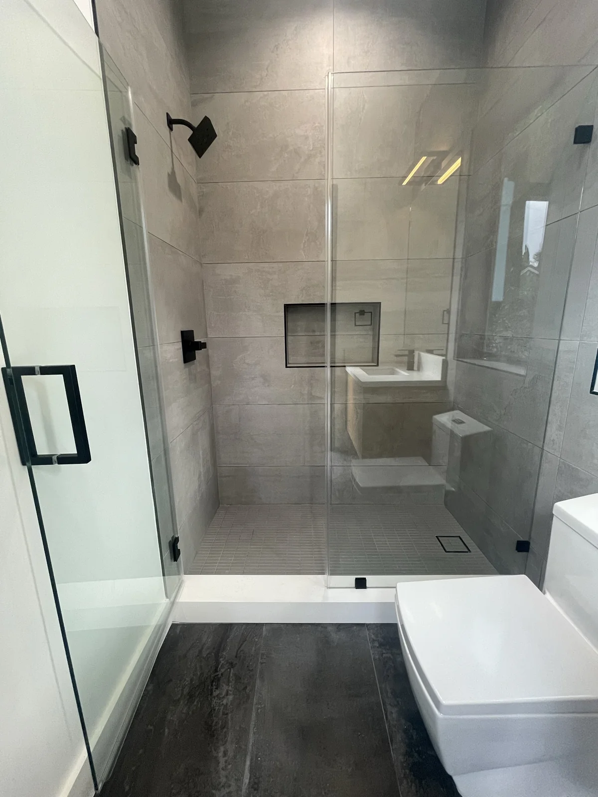 Gray tile walk-in shower with black hardware, framed glass and recessed niche