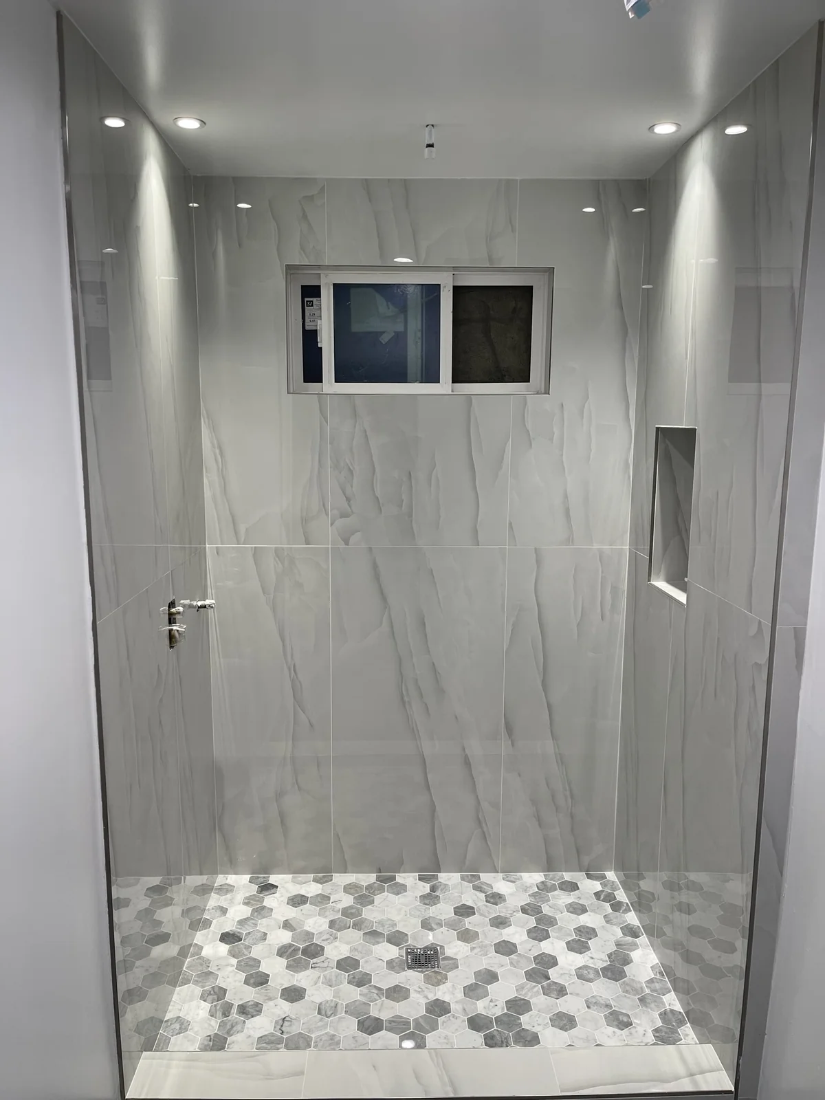 Walk-in shower installation with large-format tile, recessed niche and hex mosaic floor