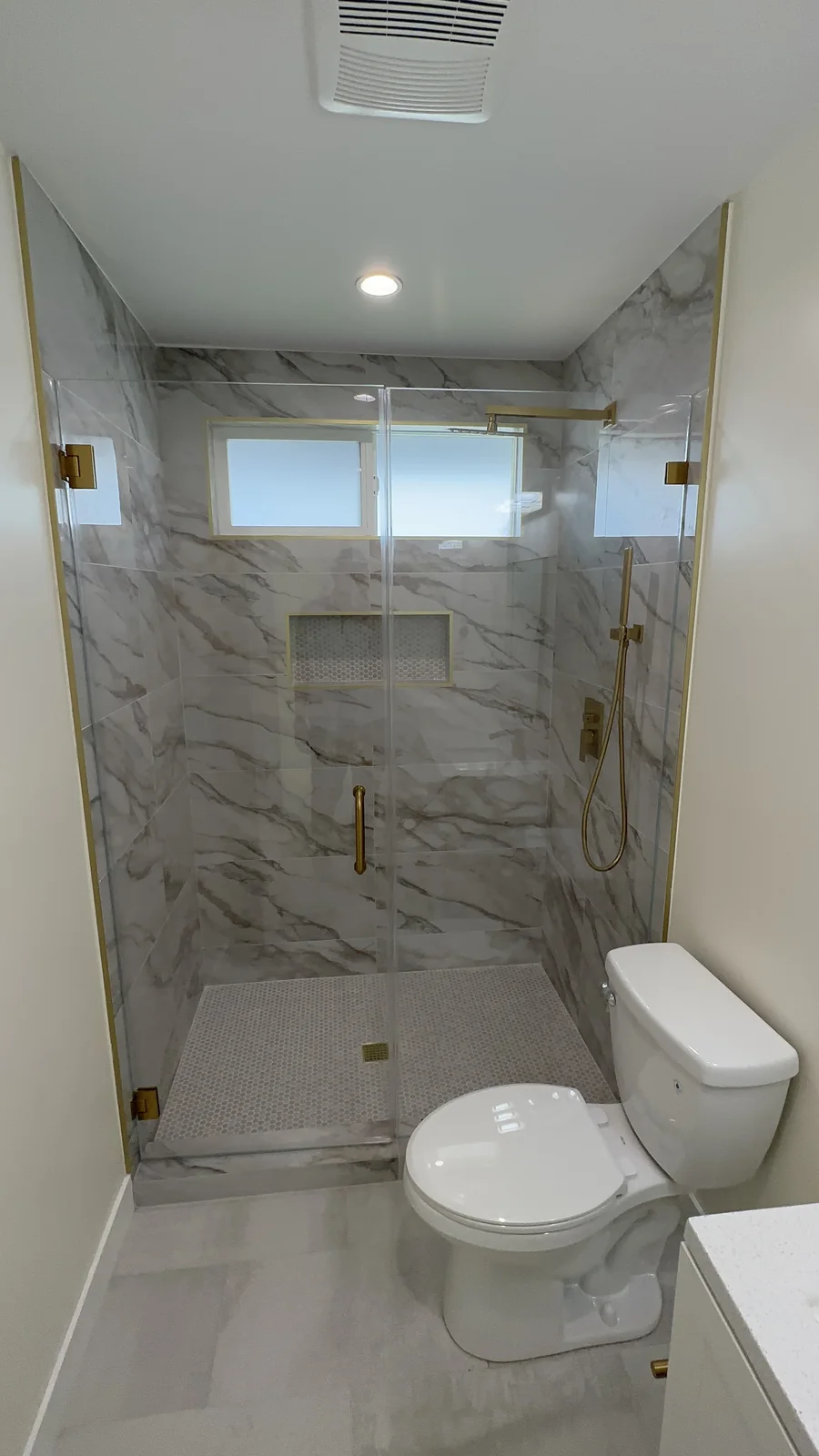 Walk-in bathroom shower with marble-look tile, clear glass enclosure, gold trim and recessed niches