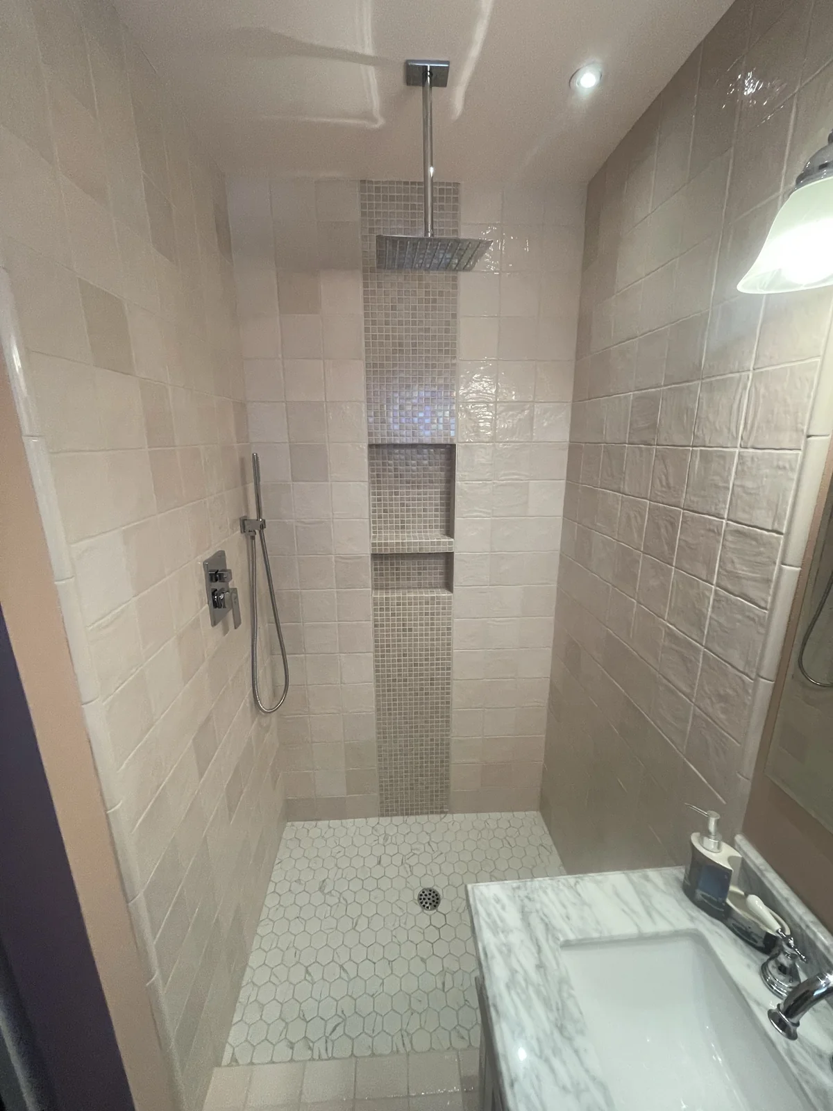 White tiled shower with mosaic accent, recessed niche and hexagonal floor tile