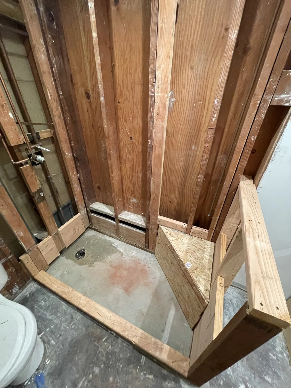 Bathroom under construction with exposed wall framing, plumbing connections and a prepared shower area