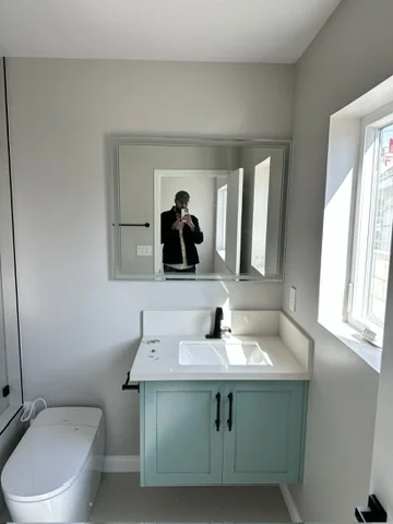 Small bathroom with pale green vanity, white countertop, framed mirror and window