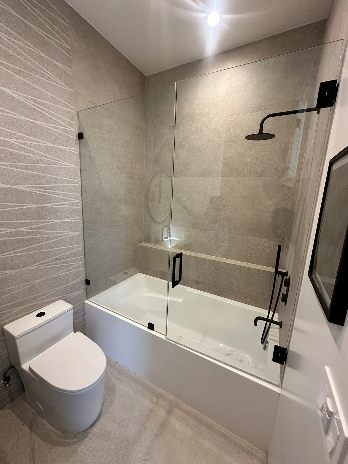 Gray tile tub and shower with black glass hardware, rainfall shower and built-in ledge