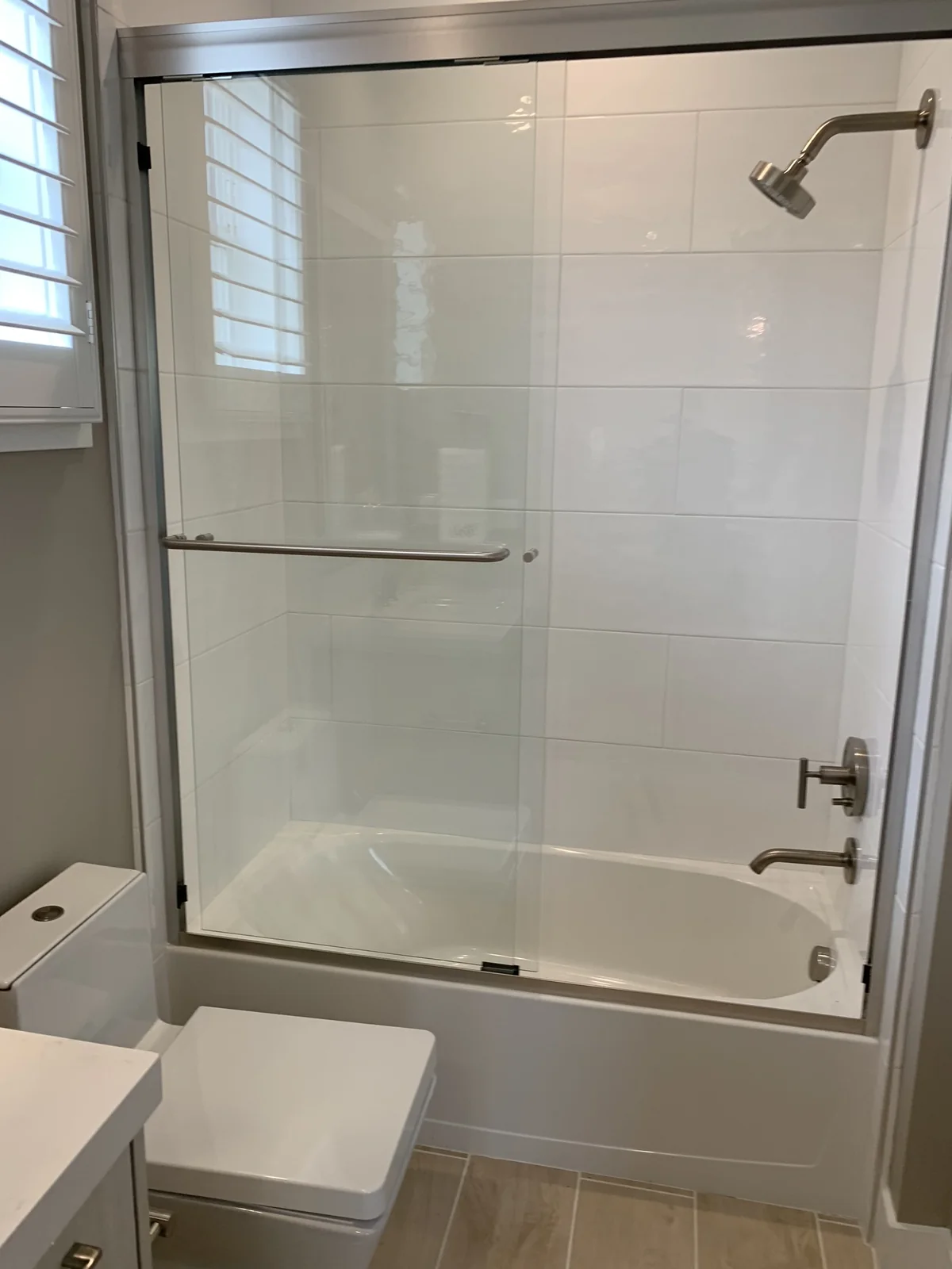 White tub and shower with glass enclosure, door hardware and wall tile