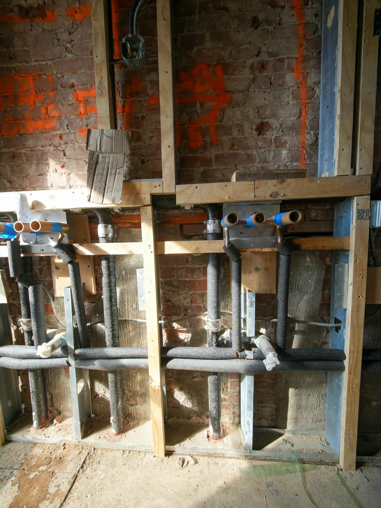 Exposed supply and drain piping and electrical conduit within an unfinished wall.