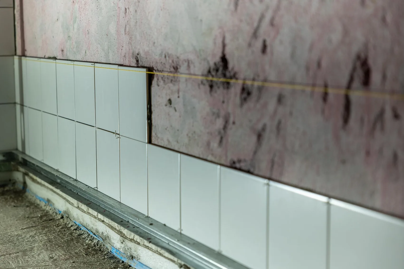Partially installed white wall tiles with spacers and a guide line during renovation.