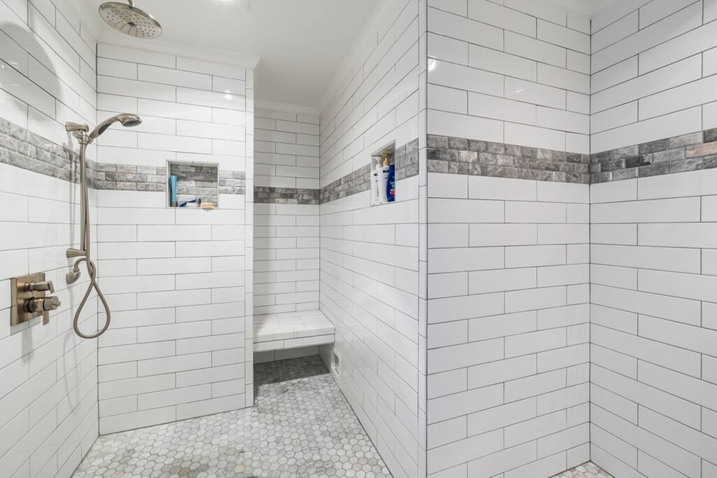 Bright white and gray tiled shower with a mosaic floor and built-in niche, illustrating a clean curbless-style finish palette.