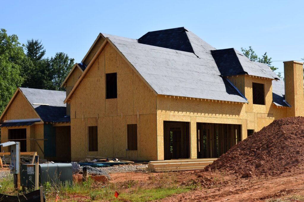 Wood-sheathed house under construction with exposed lumber openings and an empty site.