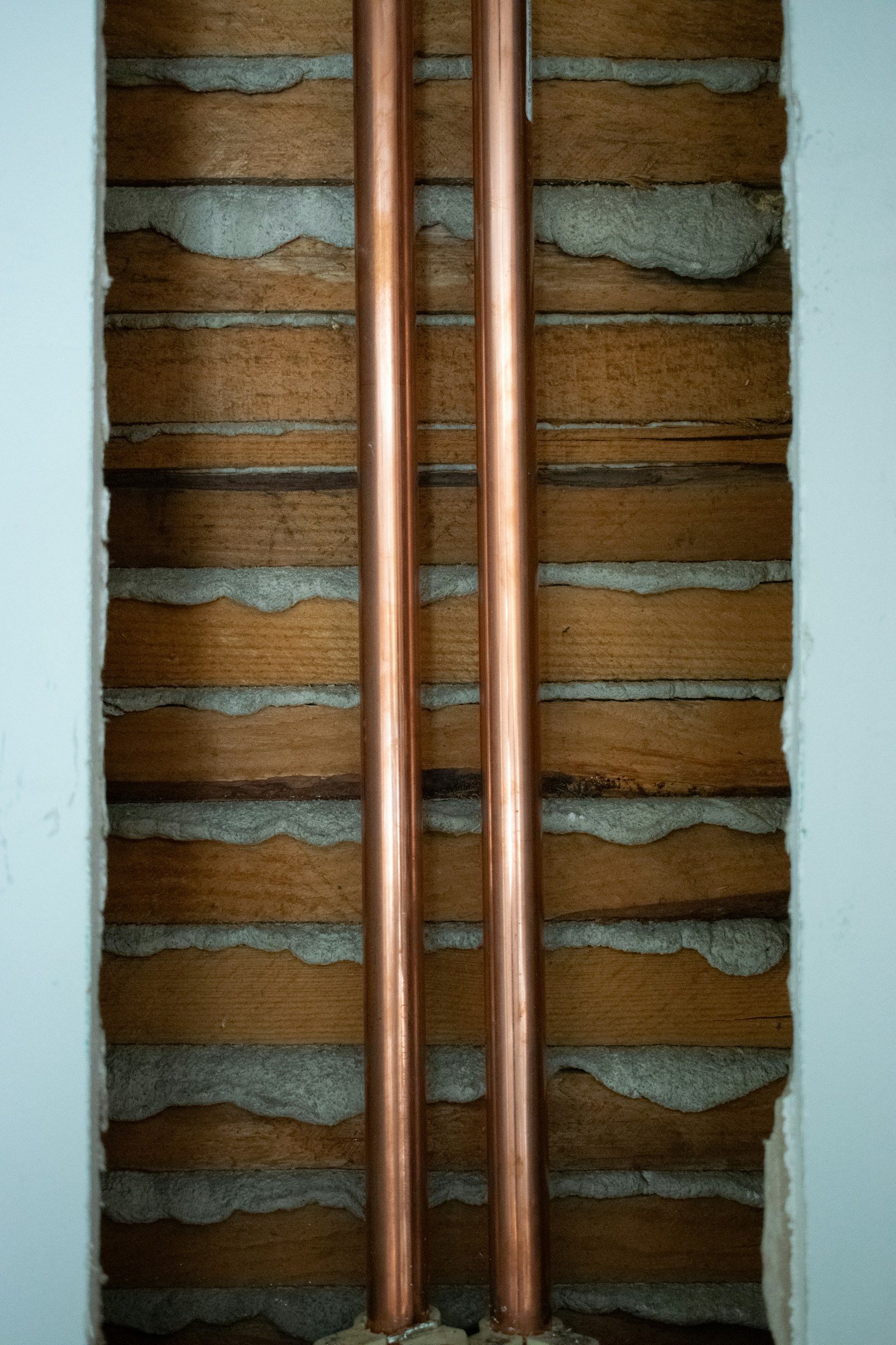 Two copper pipes exposed in a wood-lath and plaster wall