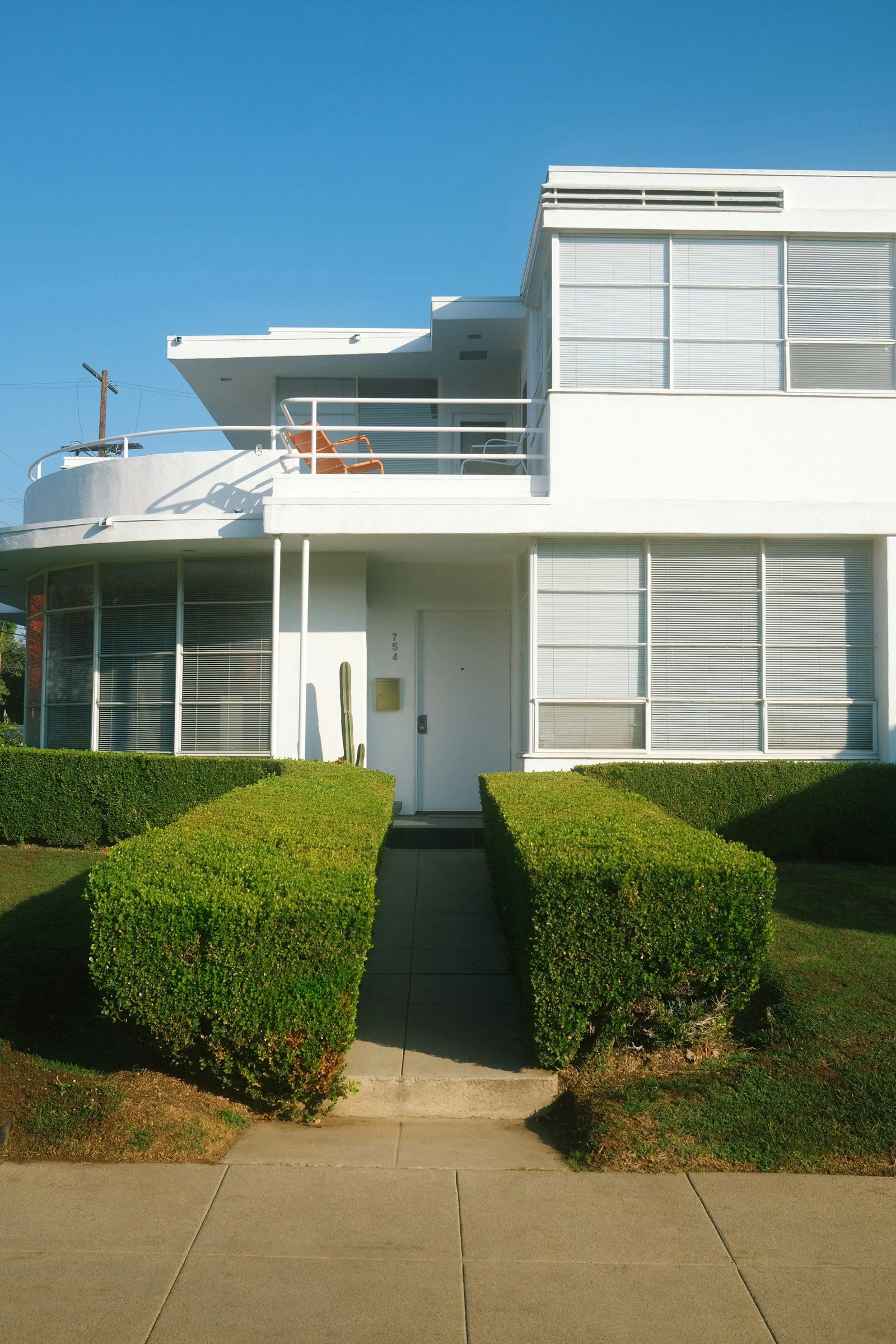 White residential exterior with broad windows, hedges and a narrow entrance path