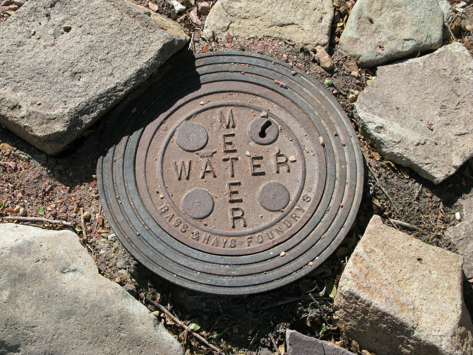 Round water-meter cover set among stones and soil