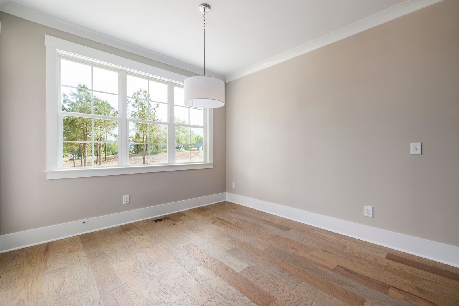 Empty room with a large window, wood flooring and a hanging light.