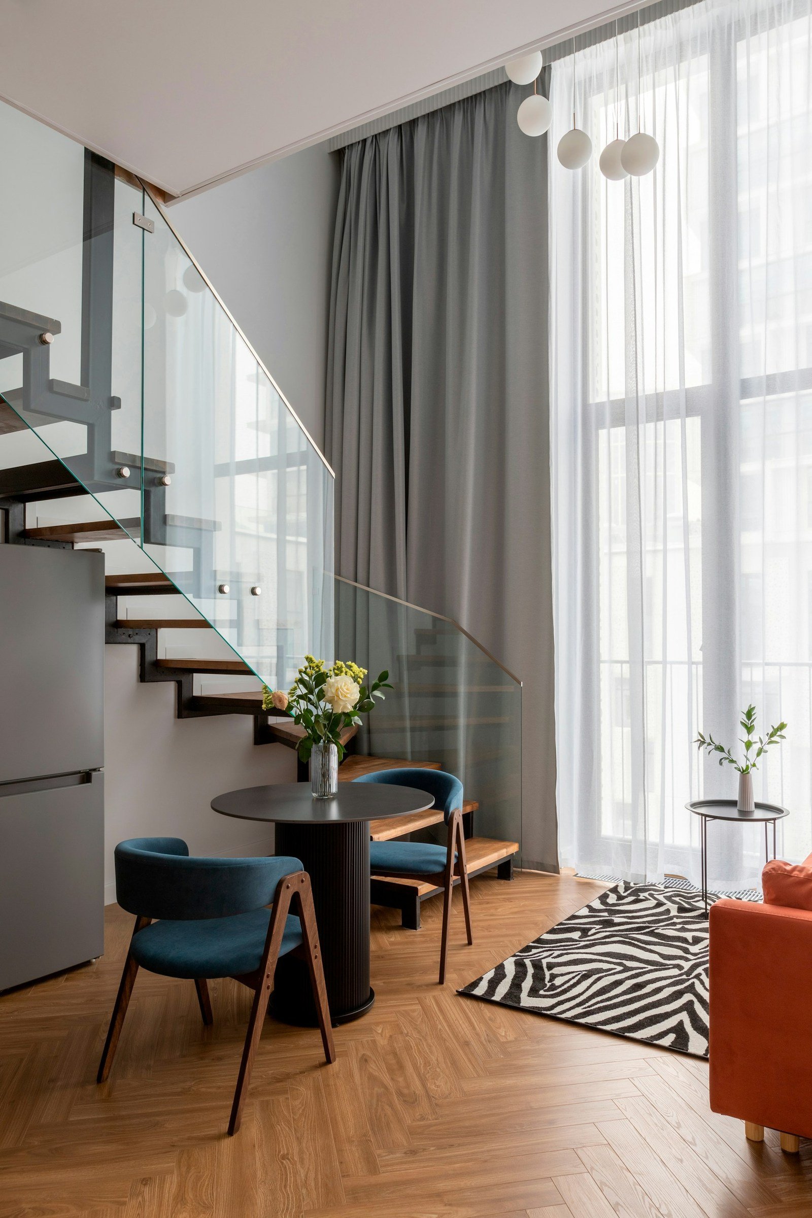 Dining space beside a glass-railed staircase and tall windows