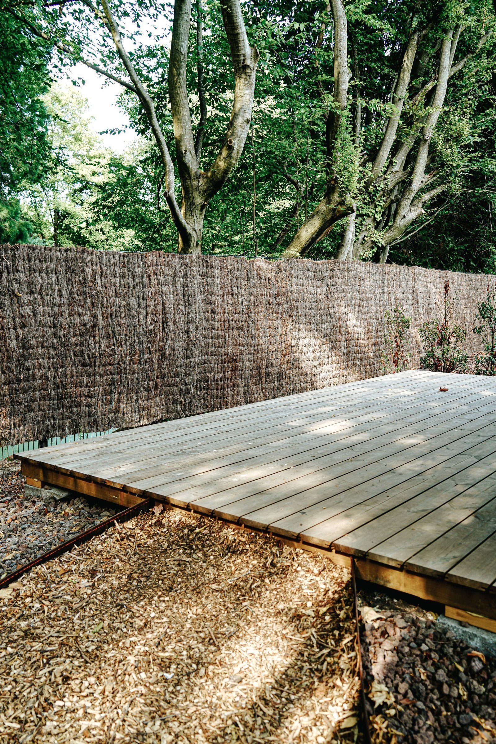 Timber garden deck beside a woven privacy screen and leafy trees