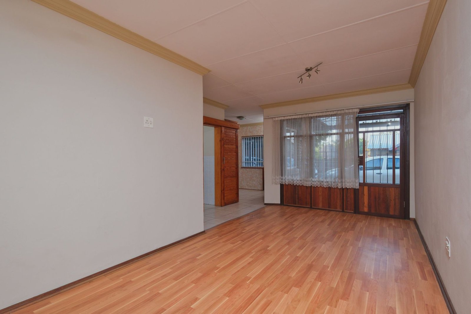 Empty room with wood-pattern flooring and a glazed entrance beside an adjoining kitchen