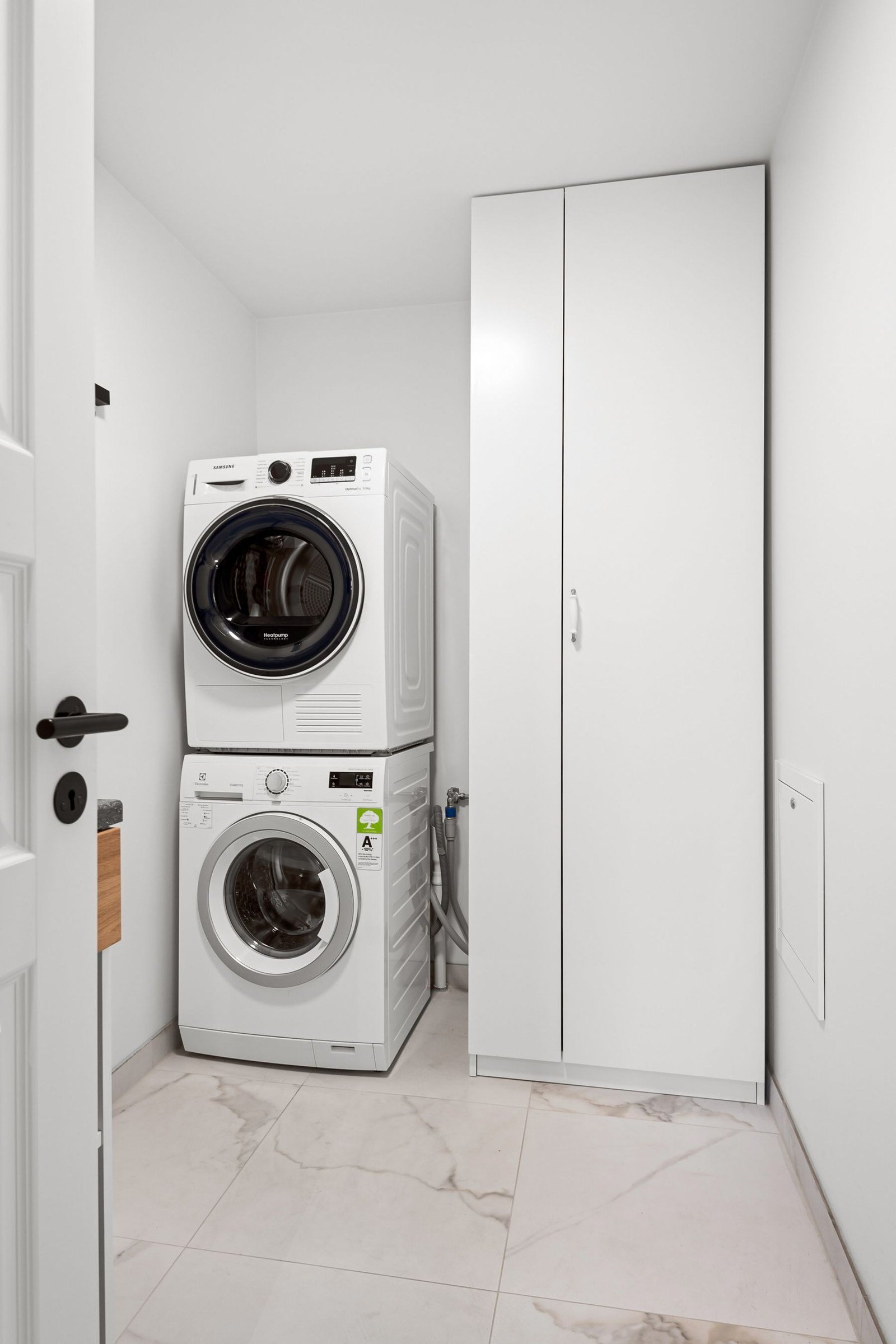 Stacked laundry appliances beside a tall white storage cabinet
