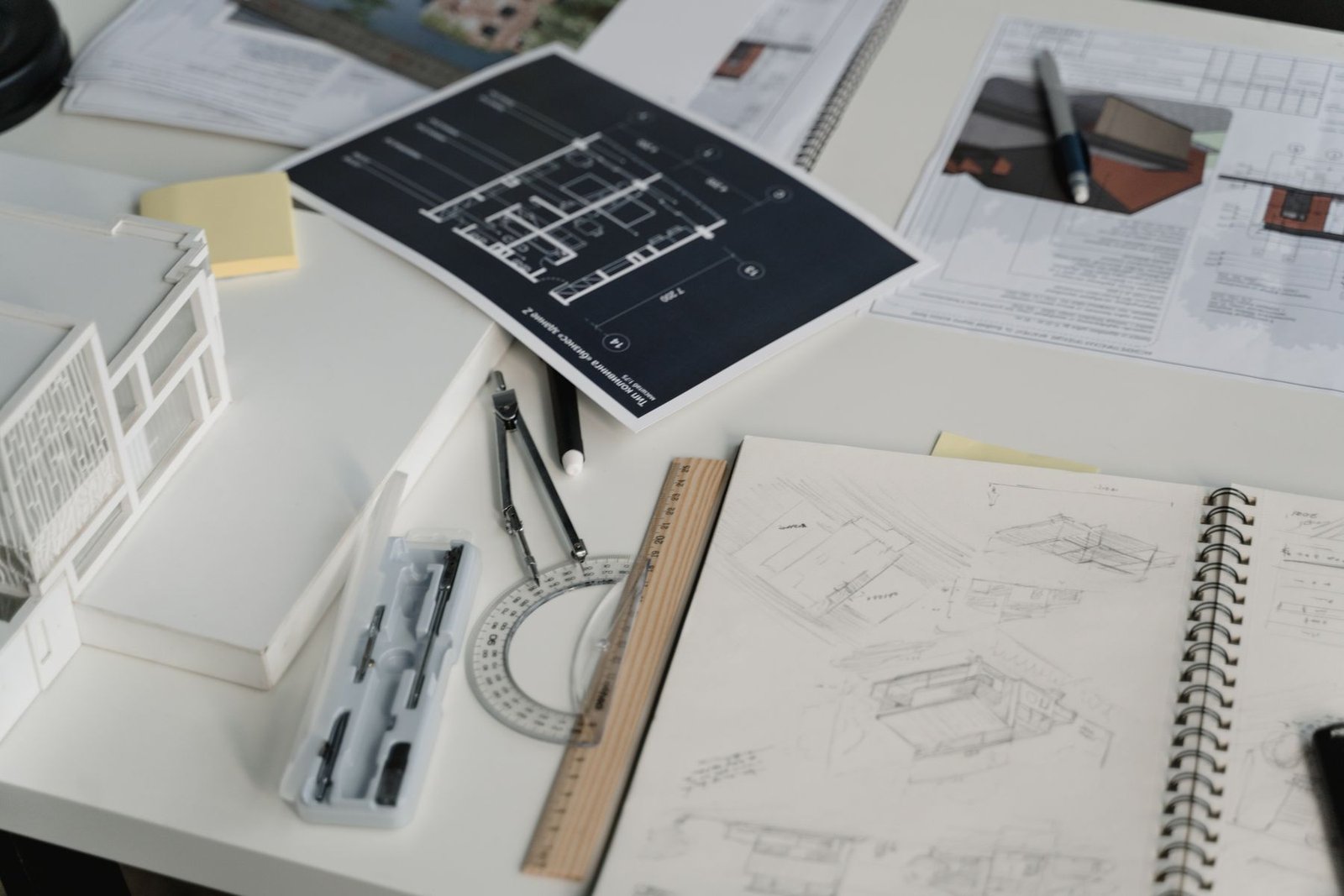 Design drawings, a small architectural model and drafting tools on a white table