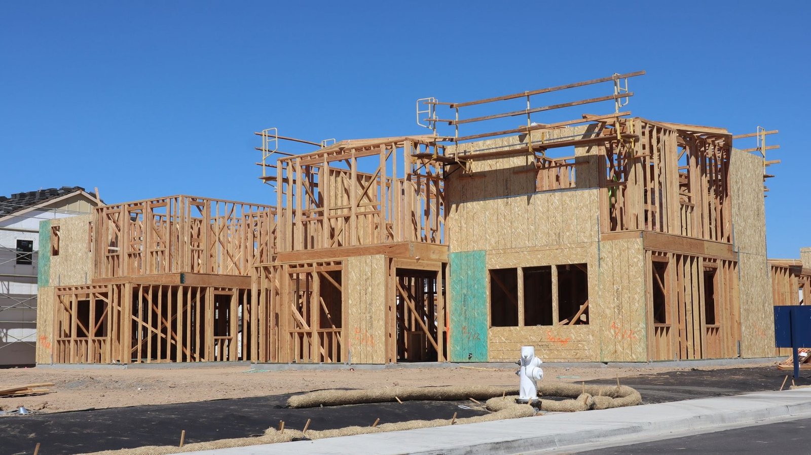 Lumber-framed houses under construction beside a bare site and street in California