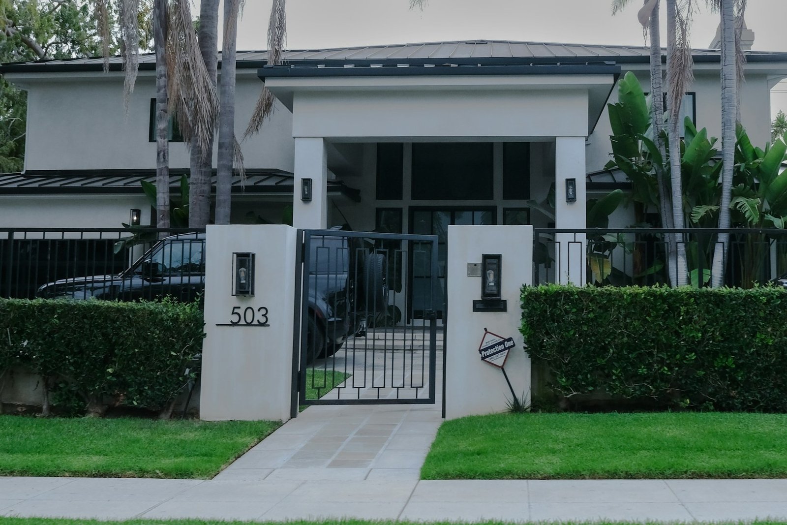 Gated residential entrance with hedges, paved walkway and palms