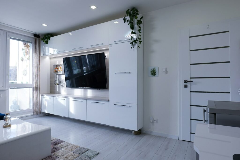 Bright apartment living area with fitted cabinets, television and a closed interior door