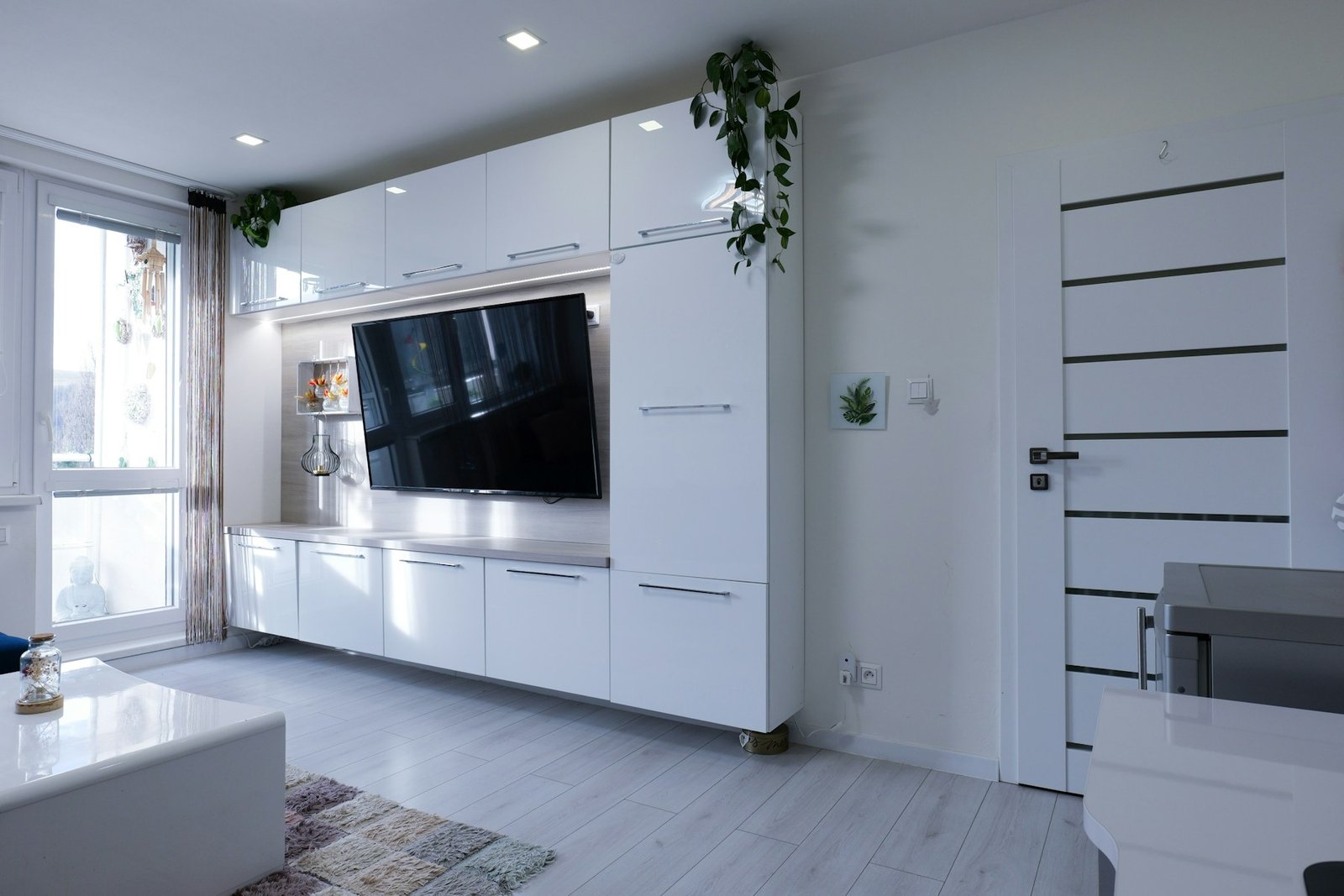 Bright apartment living area with fitted cabinets, television and a closed interior door