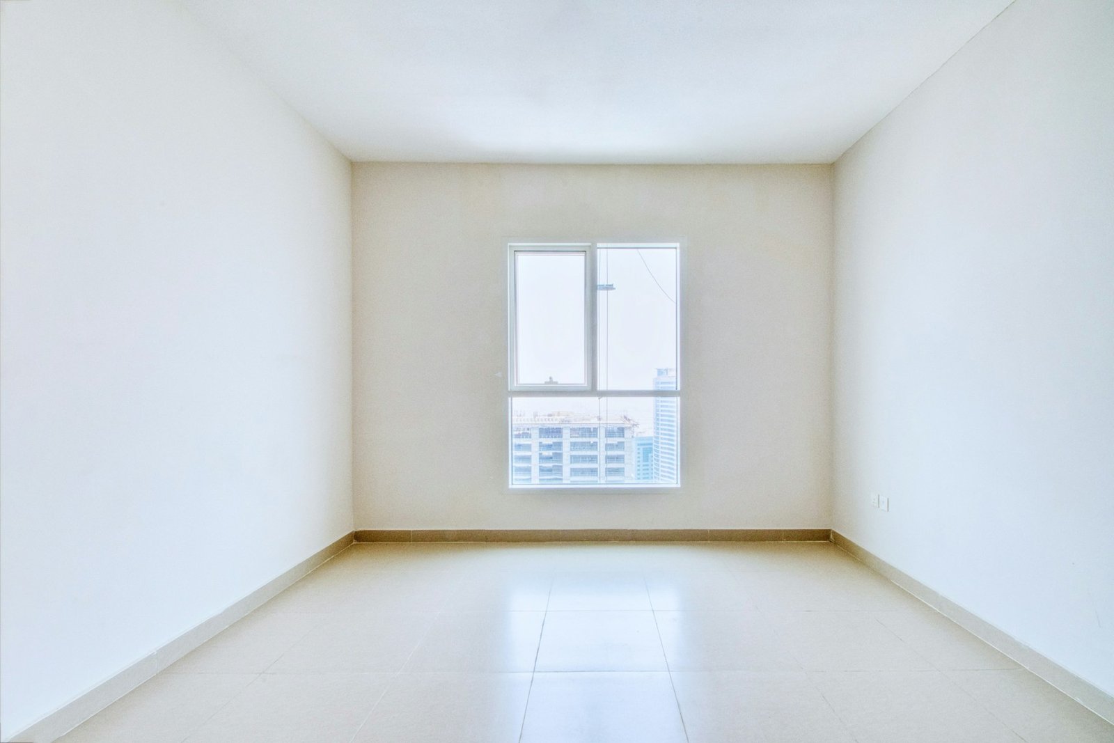 Empty apartment-style room with a tiled floor, window and white walls