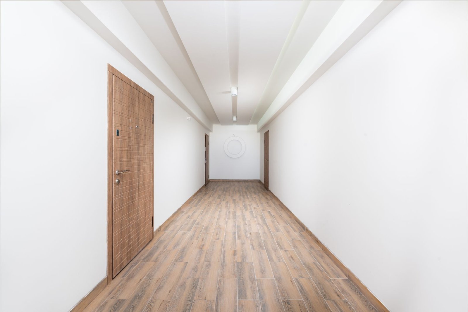 Empty finished hallway with white walls, timber doors and wood-pattern flooring
