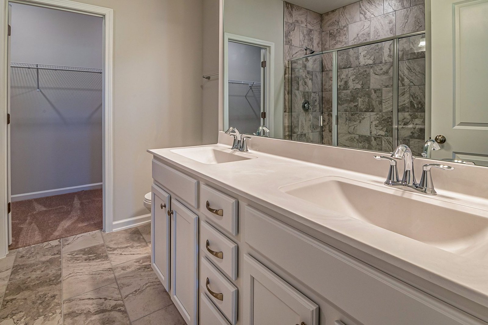 Double-sink bathroom vanity with a large mirror, glass shower and adjoining closet