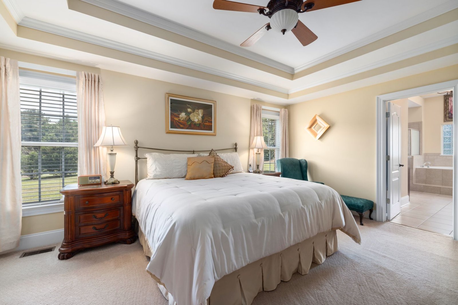 Bedroom with a tray ceiling, ceiling fan, two windows and an adjoining bathroom