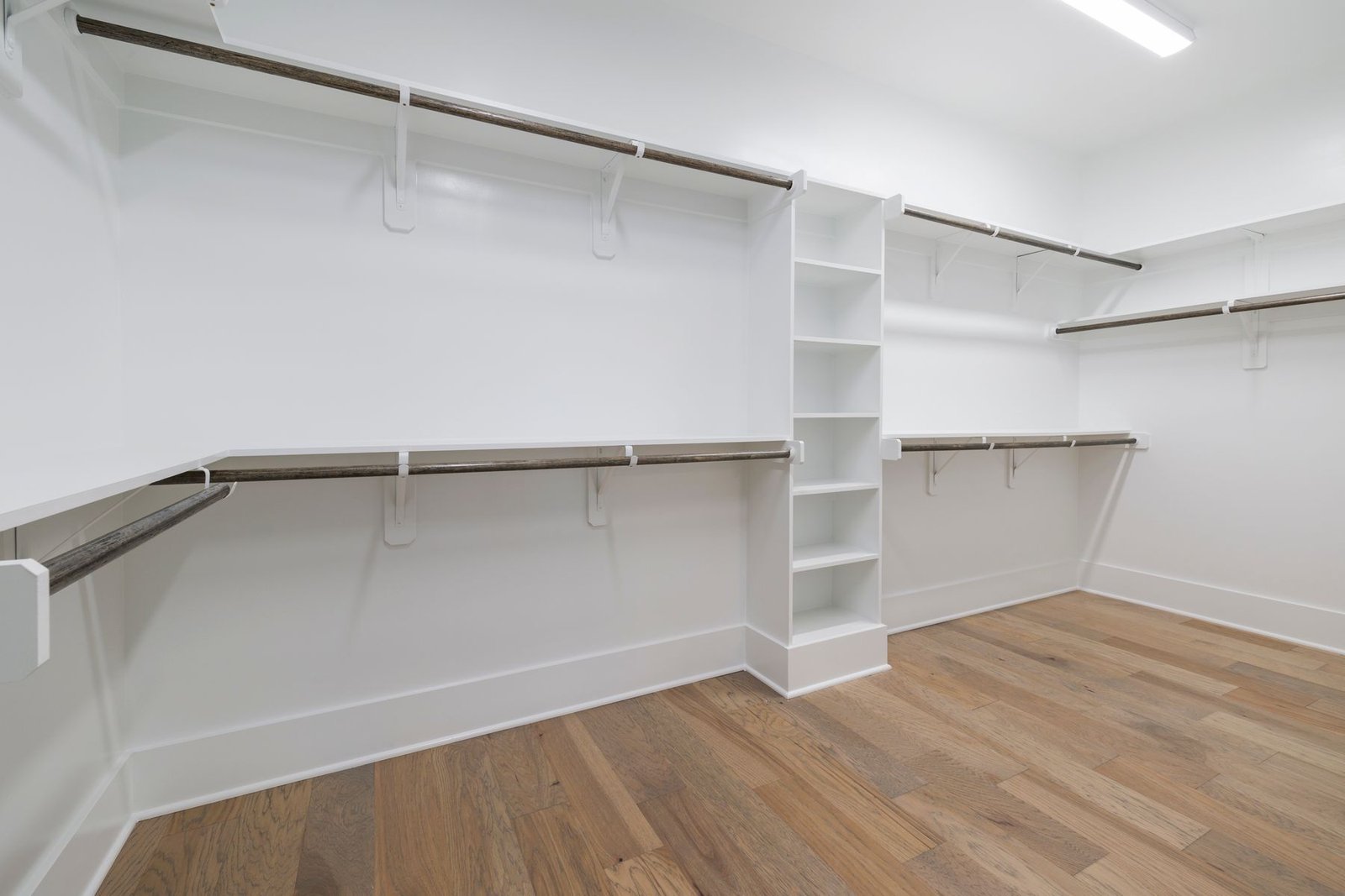 Empty walk-in closet with white shelving, hanging rails and wood-pattern flooring