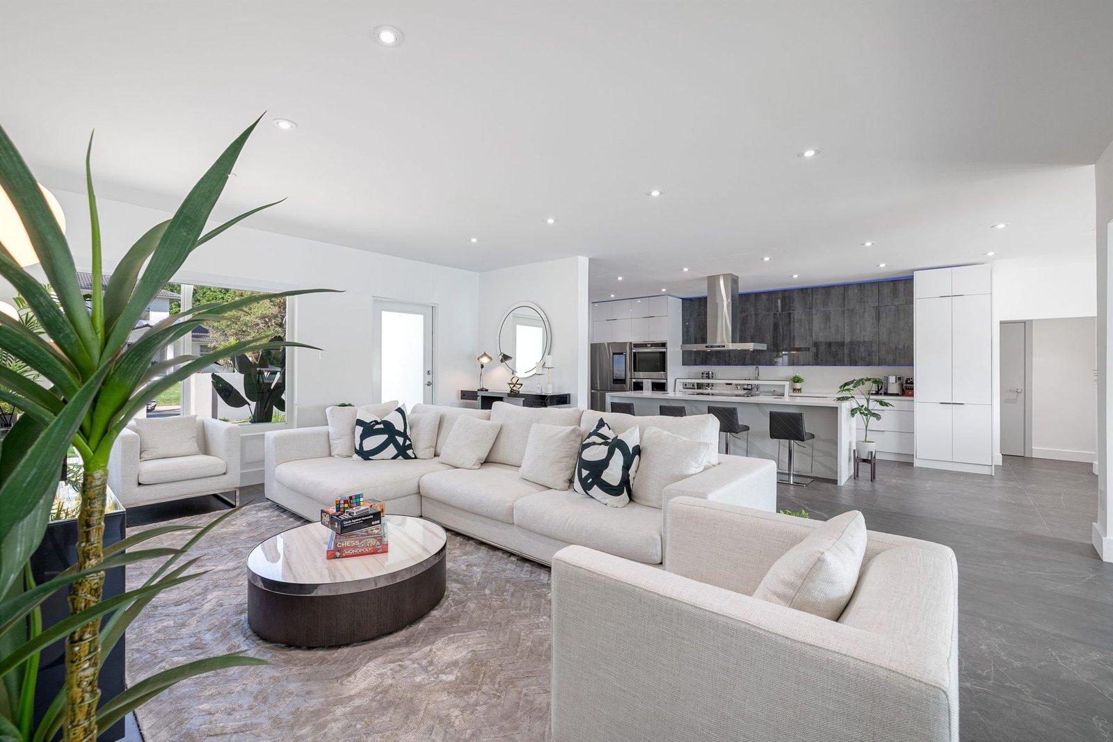 Open living area with white seating, recessed lighting and an adjoining kitchen
