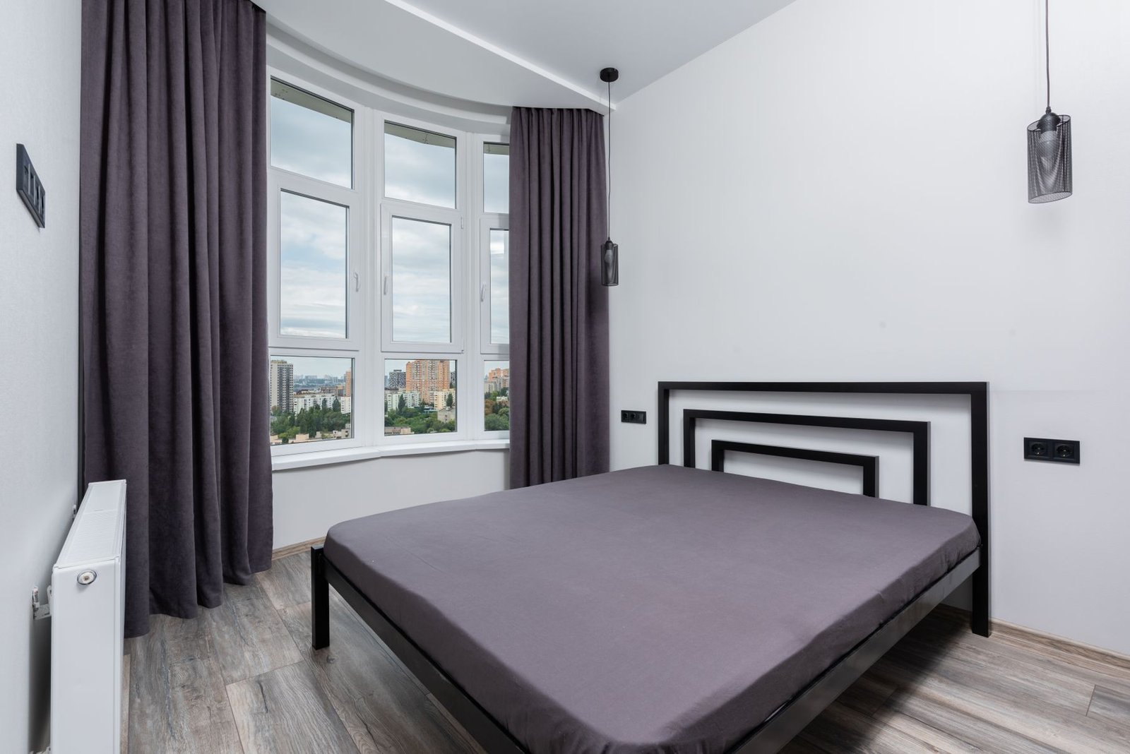 Bedroom with a curved window wall, dark curtains and a simple bed