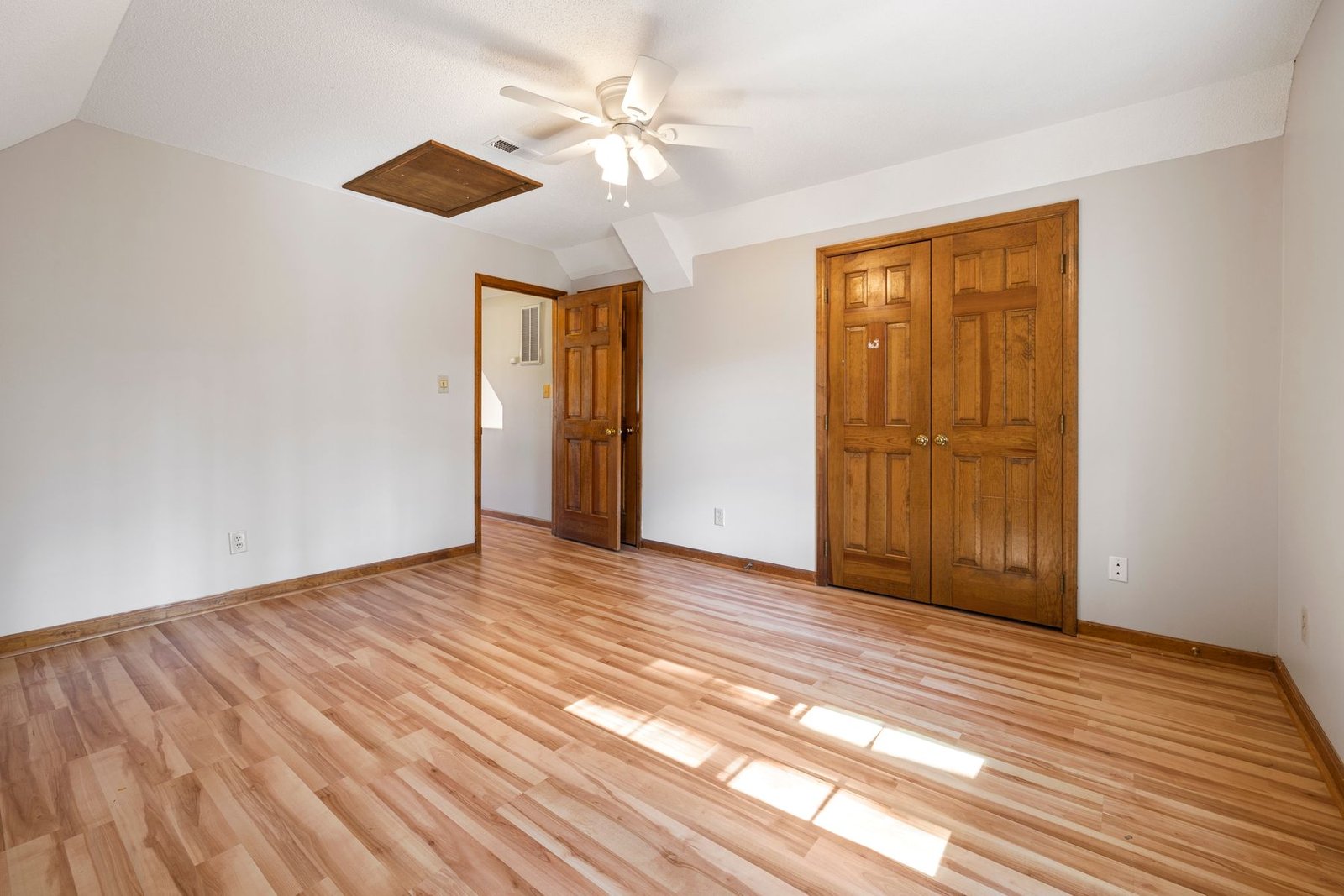 Empty bedroom with wood flooring, wood-trimmed doors and a ceiling fan.