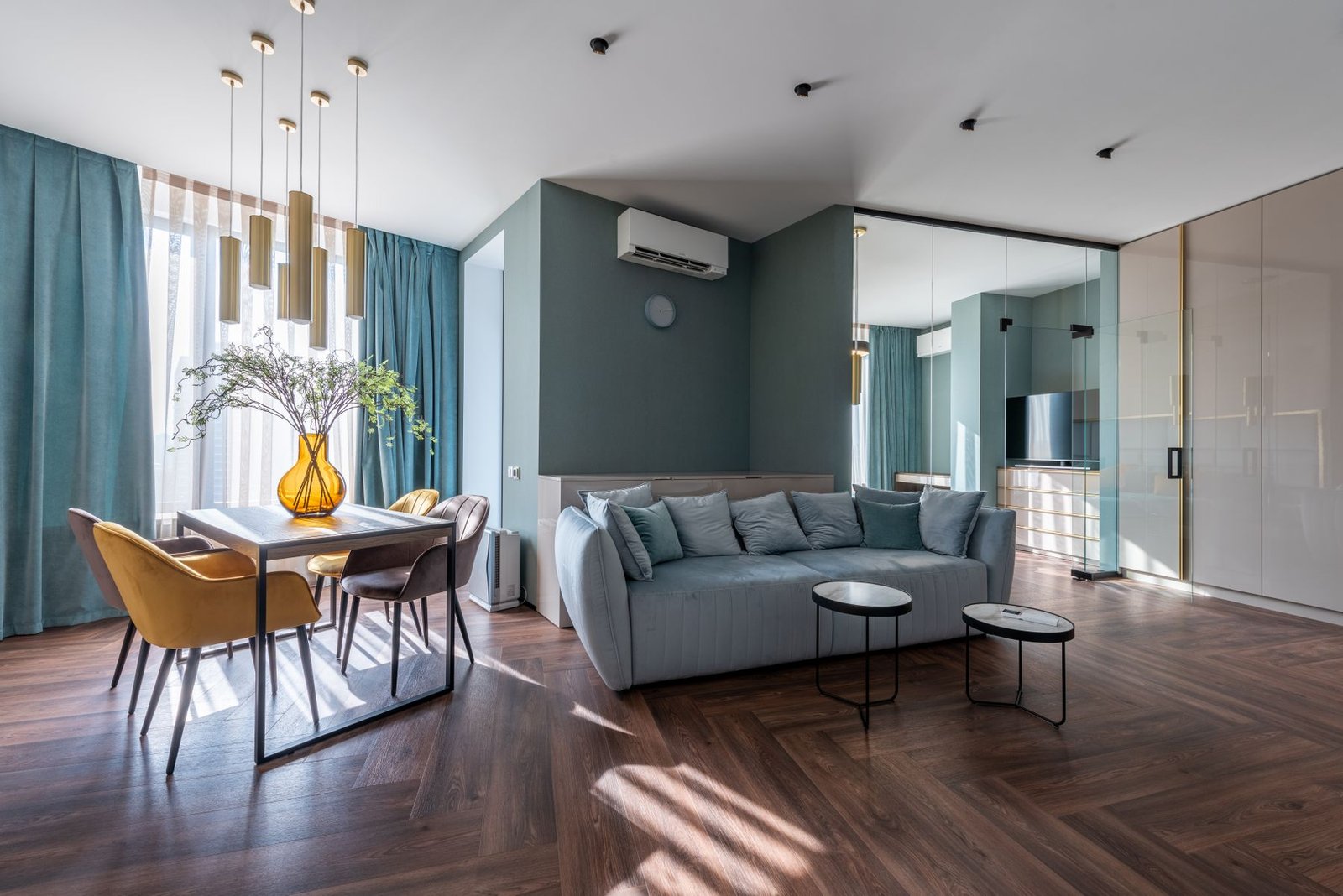 Living and dining area with wood flooring, blue-green walls and a glass room partition