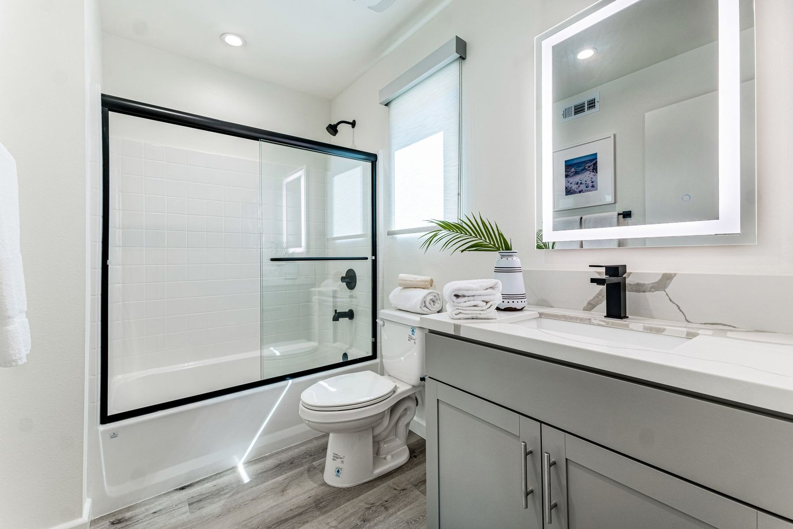 Compact bathroom with a gray vanity, toilet and glass bath screen.