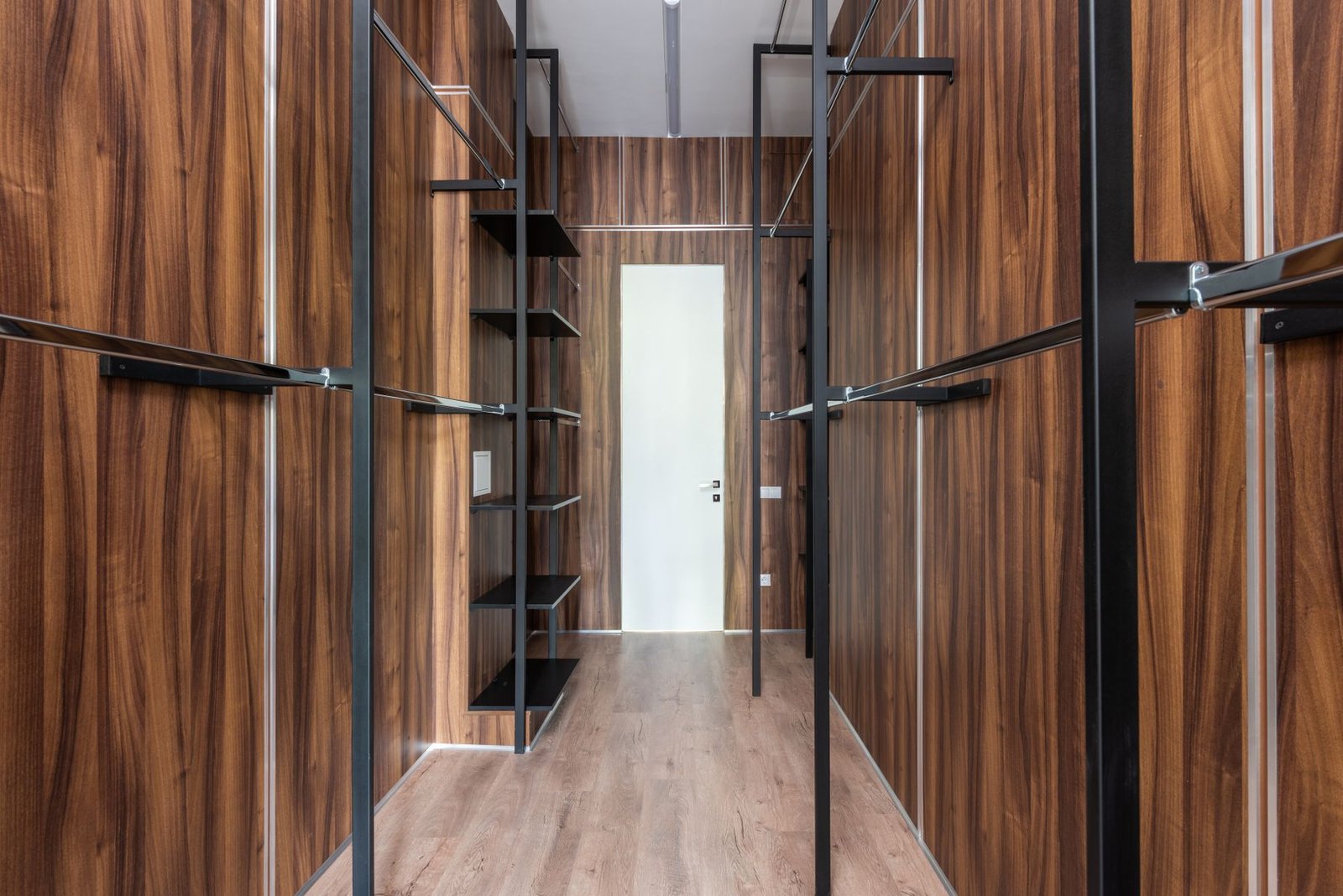 Empty wood-finished walk-in wardrobe with hanging rails and shelves.
