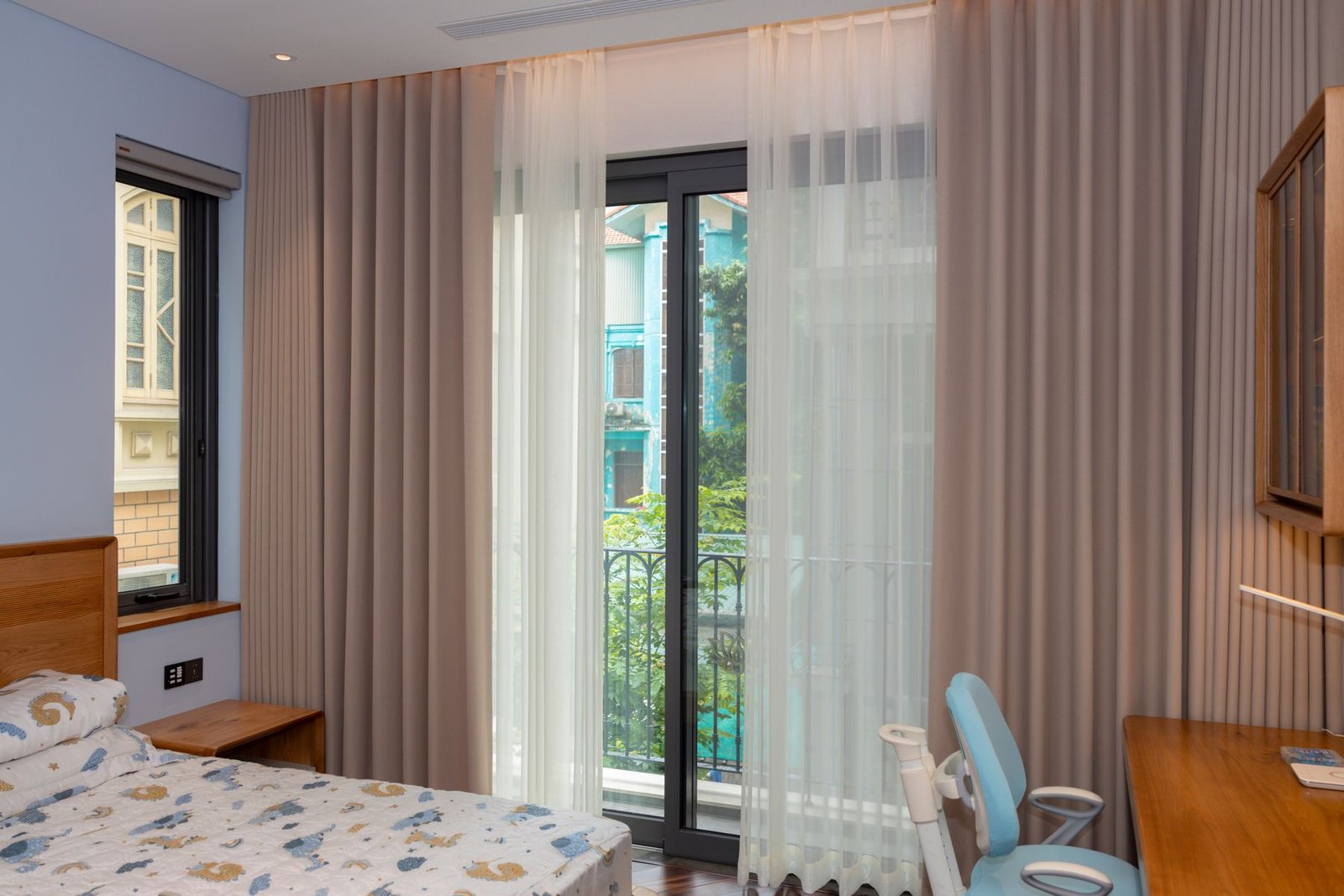 Bedroom with a small bed, wood desk, curtains and balcony doors.