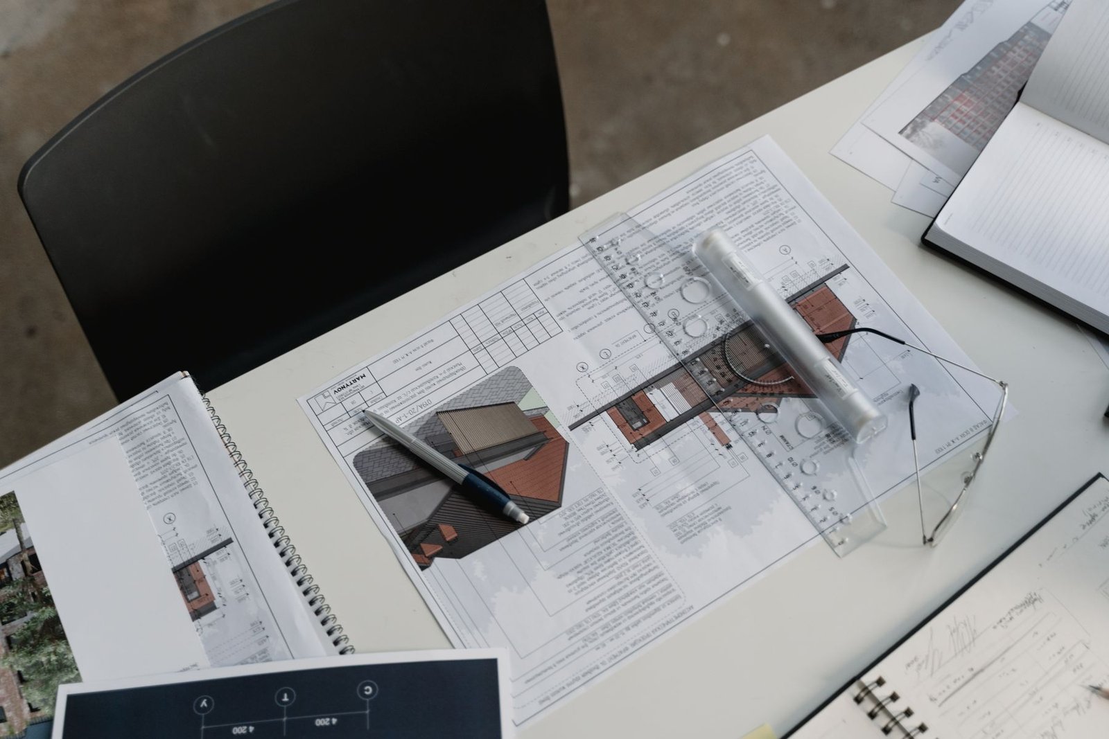 Design papers, a ruler, eyeglasses and a pen on a work surface.