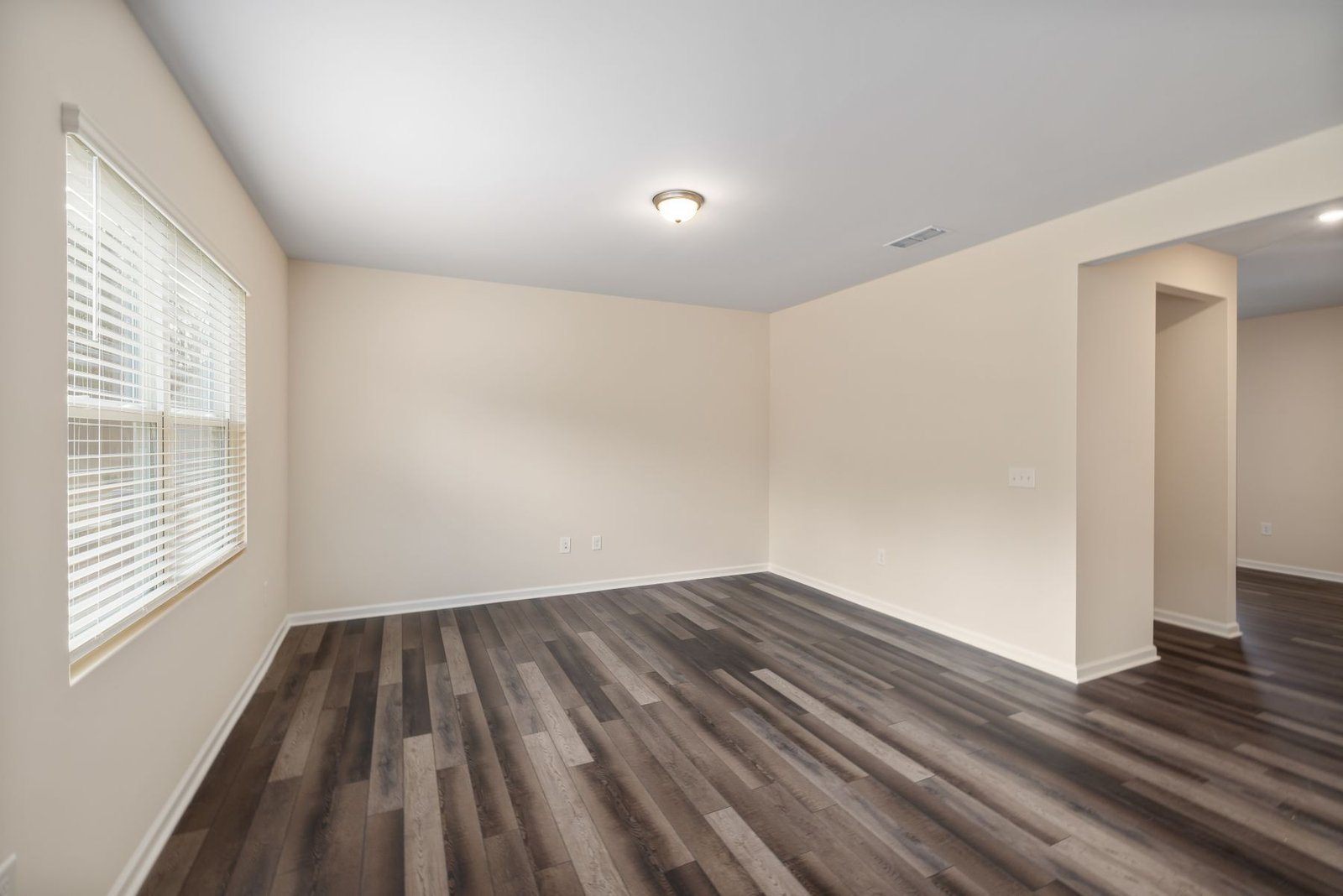 Empty room with gray wood-pattern flooring and a broad opening to another space.