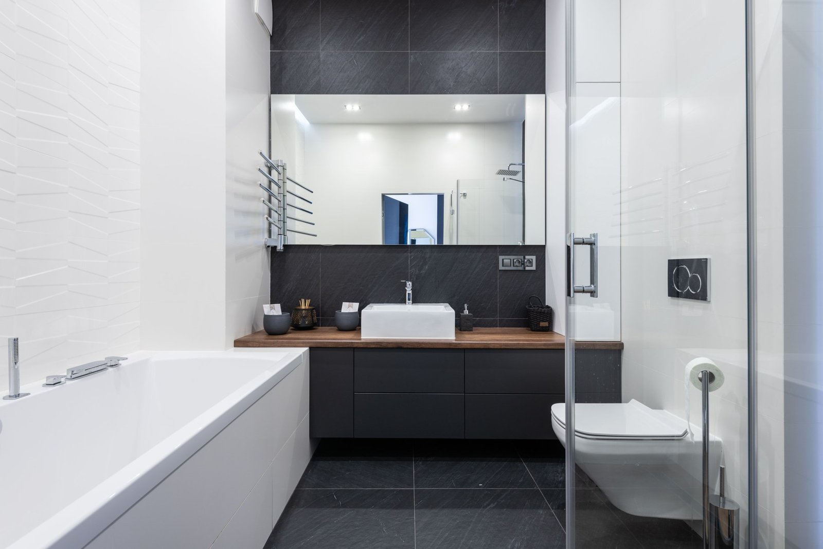 Black and white bathroom with bathtub, vanity mirror, glass shower and toilet