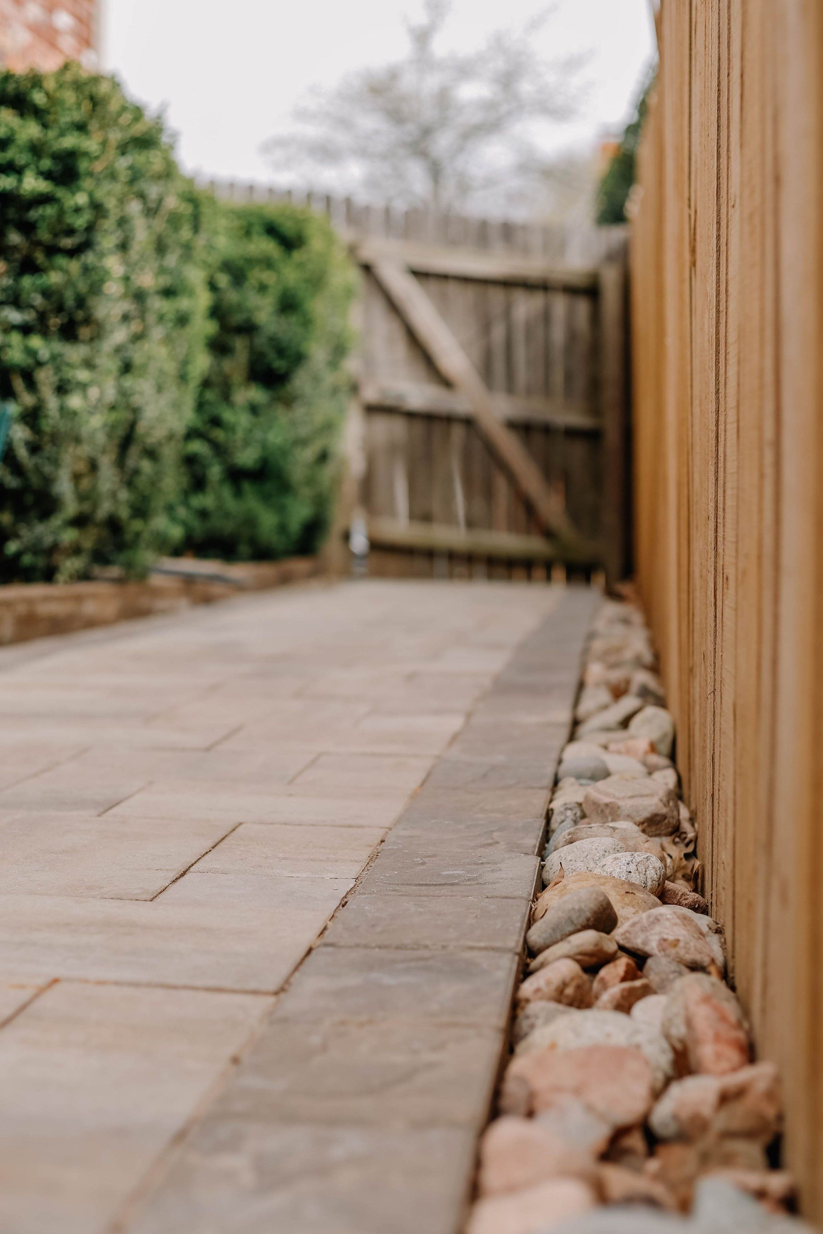 Paved garden path leading to a closed wooden gate beside a timber fence