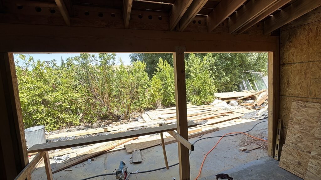 Wide wood-framed opening with temporary lumber, hoses and stored construction material outside
