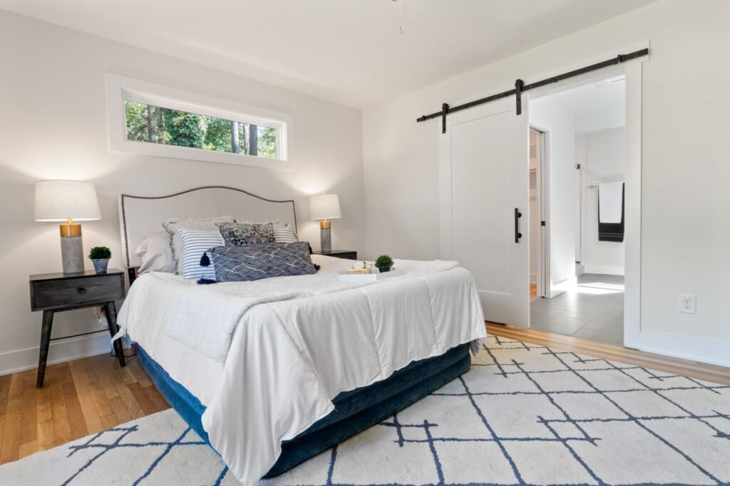 Bedroom with a bed, high window and sliding door opening toward a bathroom
