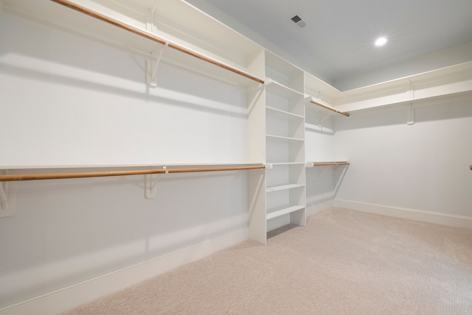 Empty walk-in closet with wooden hanging rods and white shelves