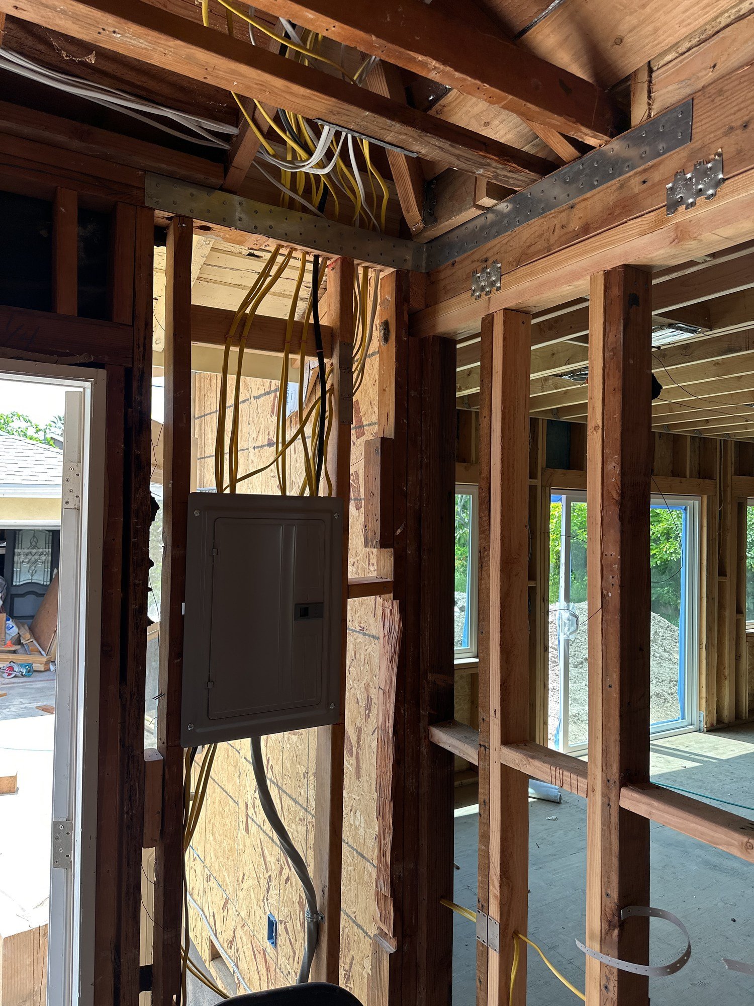 Electrical panel and cabling beside a wood-framed opening and exposed ceiling members